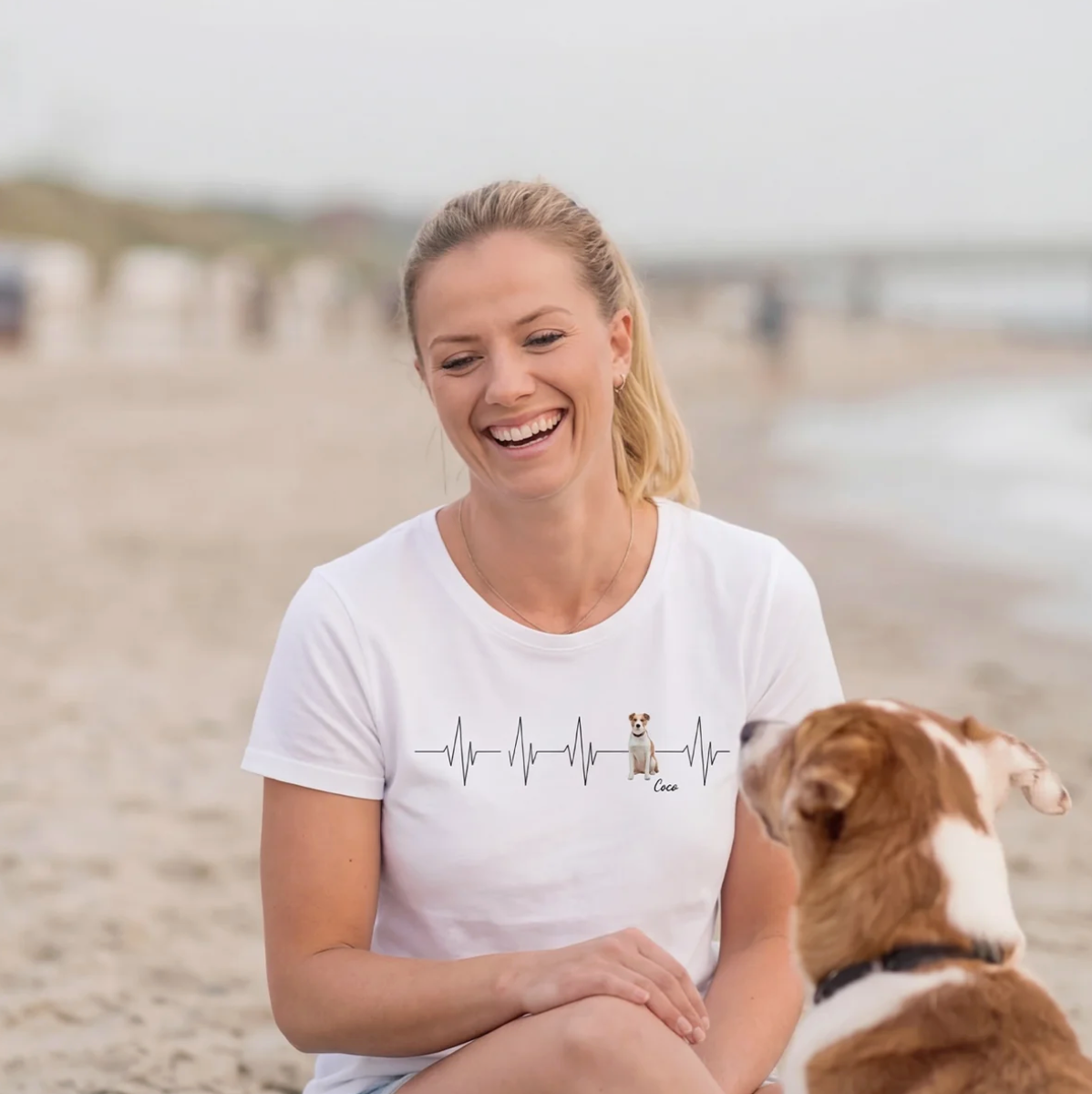White T-shirt with heartbeat pattern and dog motif, woman sitting on the beach.