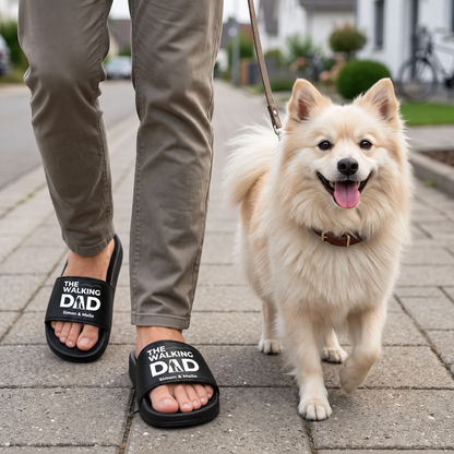 Person wearing personalized black slides with "THE WALKING DAD" print, walking a dog.